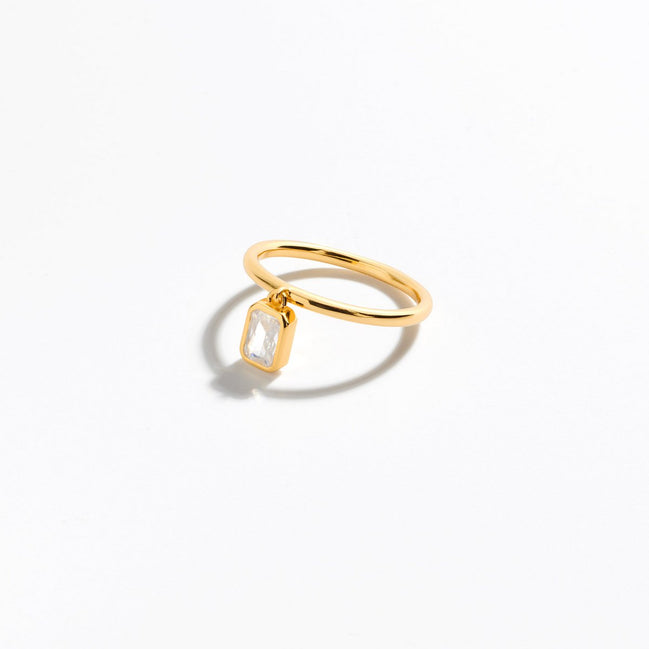 vergoldeter Ring mit baumelnden Zirkoniastein im Baguetteschliff, der am Ring befestigt ist