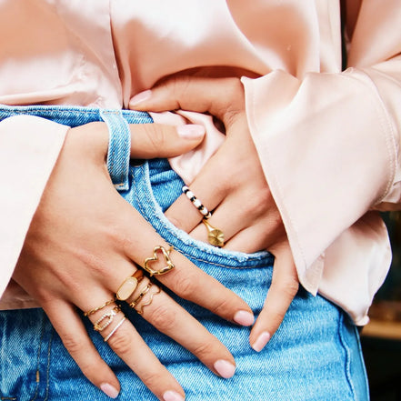 Goldfarbener Siegelring mit runder Front und feiner Sonnenschliff Struktur, kombiniert mit weiteren Ringen und Jeans