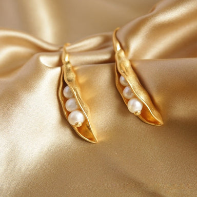 Paar goldfarbener Pea-Pod-Ohrringe mit weißen Perlen, arrangiert auf goldenem Satin
